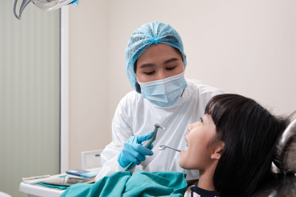 Asian female pediatric dentist checks and examines a little Thai girl's caries teeth in dental clinic, well-being mouth oral hygiene, and professional orthodontic healthcare work in a kid hospital.