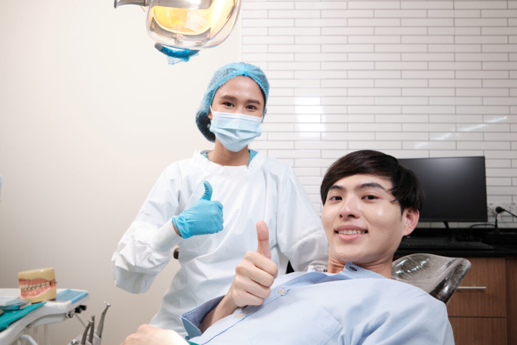 Portrait of Asian female dentist and male patient thumbs up, tooth whitening implant, happy smile, and looking at camera in dental clinic, mouth hygiene healthcare work in a doctor's hospital.